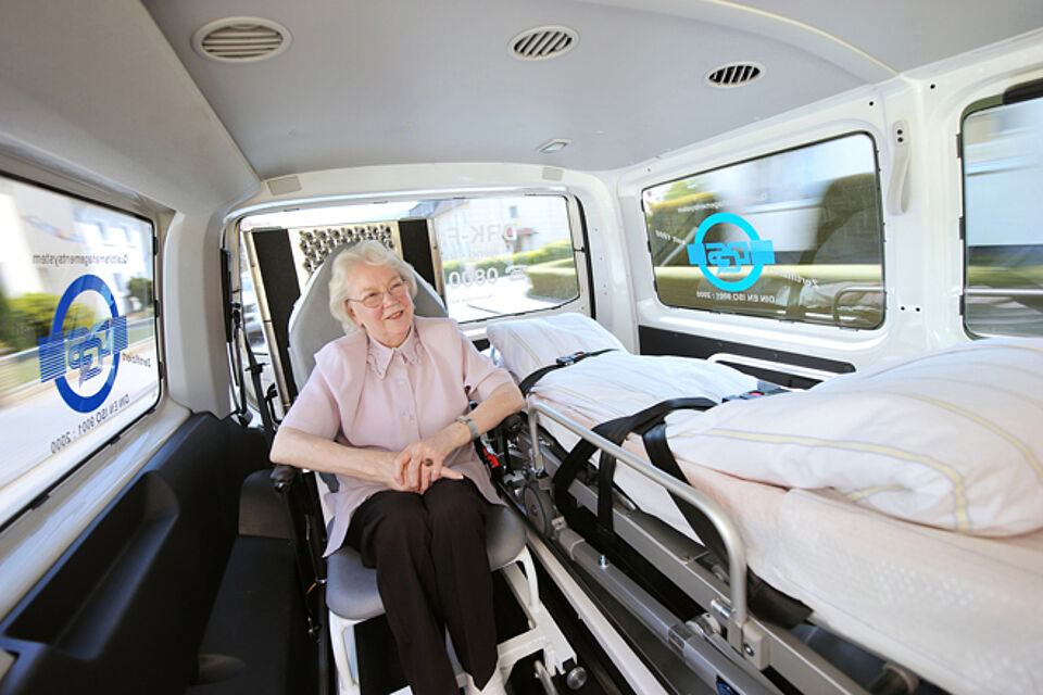 Eine ältere Dame im Rollstuhl in einem Fahrdienst Fahrzeug