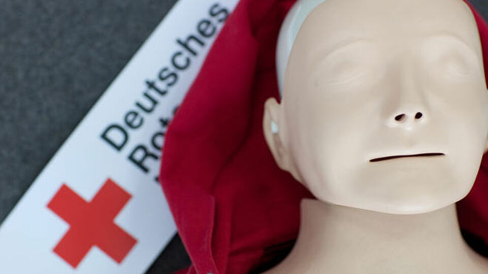 Kopf einer Puppe zum Üben mit DRK Logo links daneben