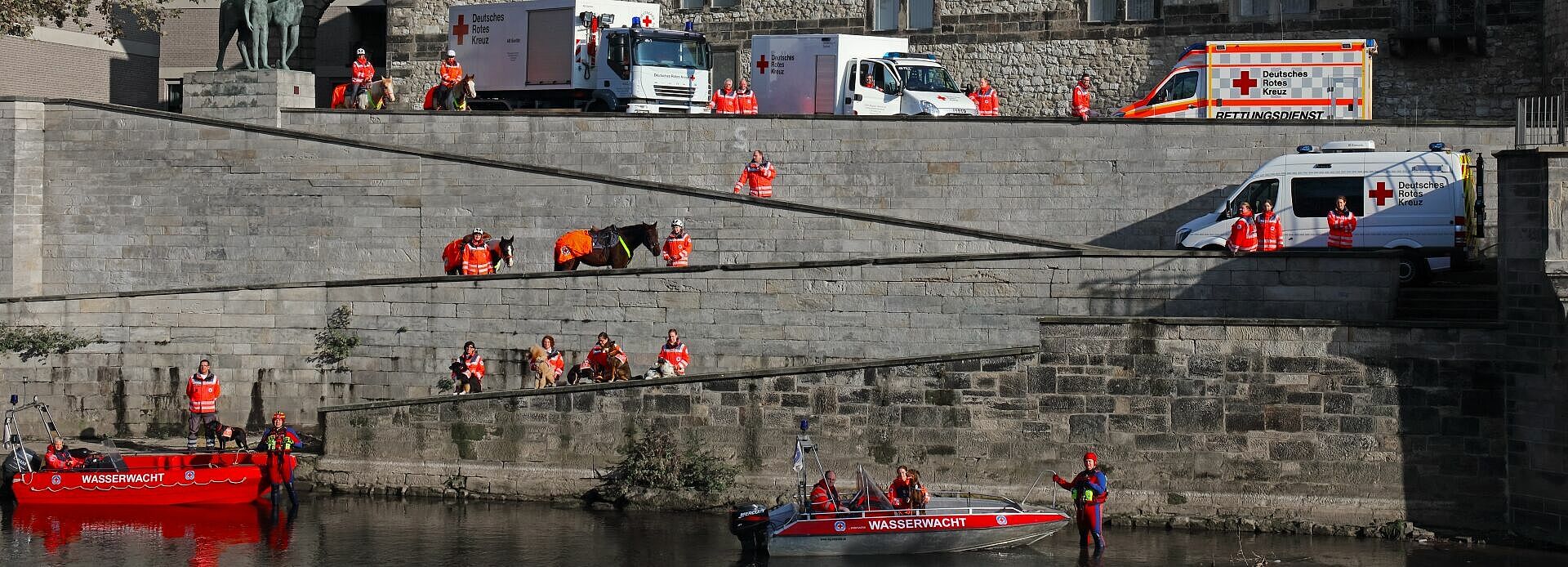 Einsatzkräfte des Deutschen Roten Kreuzes und der Wasserwacht stehen mit Einsatzfahrzeigen, Booten und Pferden am Leineufer Hannover.